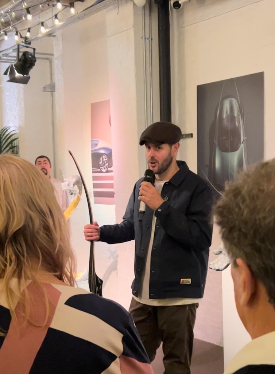 Ian Edwards holding a traditional longbow while speaking to a gallery audience