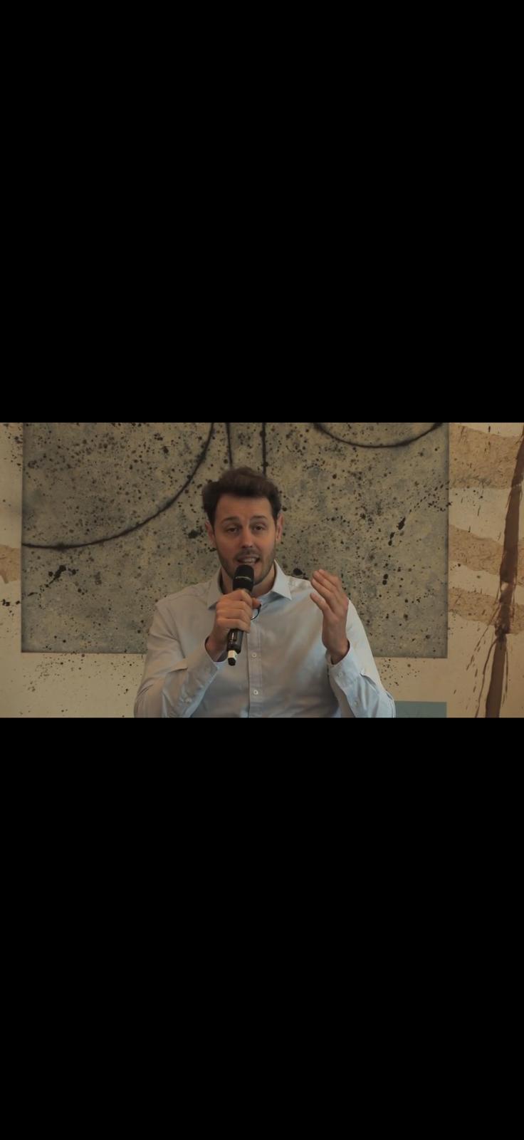 Close-up of Ian Edwards speaking with a microphone in front of one of his paintings