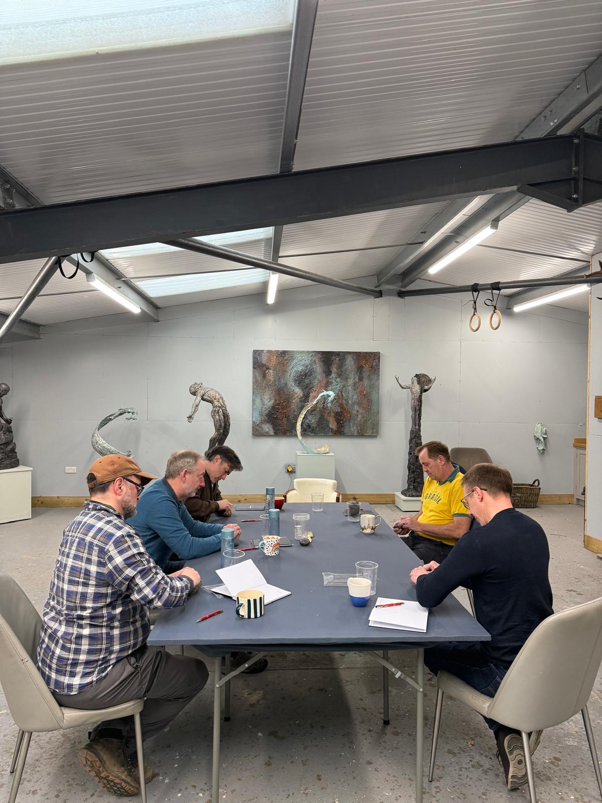 A senior team seated around a table in Ian Edwards' working sculptor's studio, surrounded by bronze sculptures